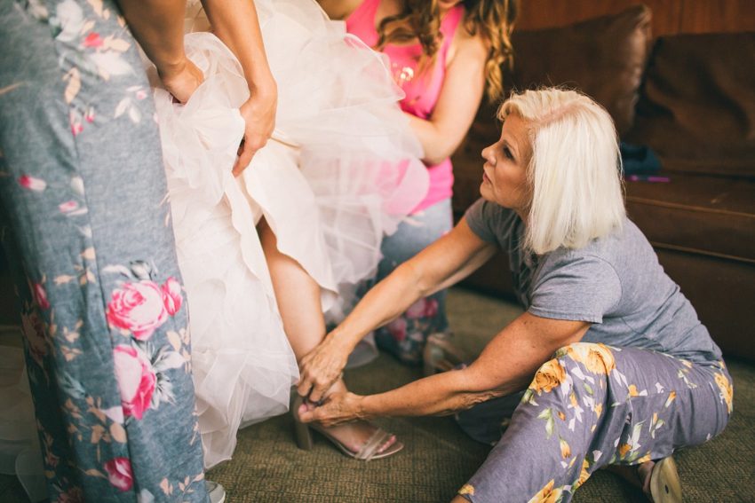 Mother of Bride helping bride get her wedding shoes on